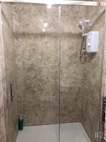 A walk-in shower with a glass door, beige tiles, and a handheld showerhead.