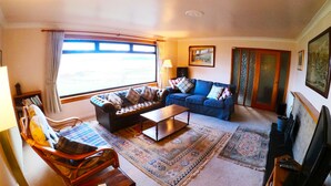 A living room with a sofa, armchair, coffee table, and a television. - Steading Holidays - Ardvaig (Acharacle)