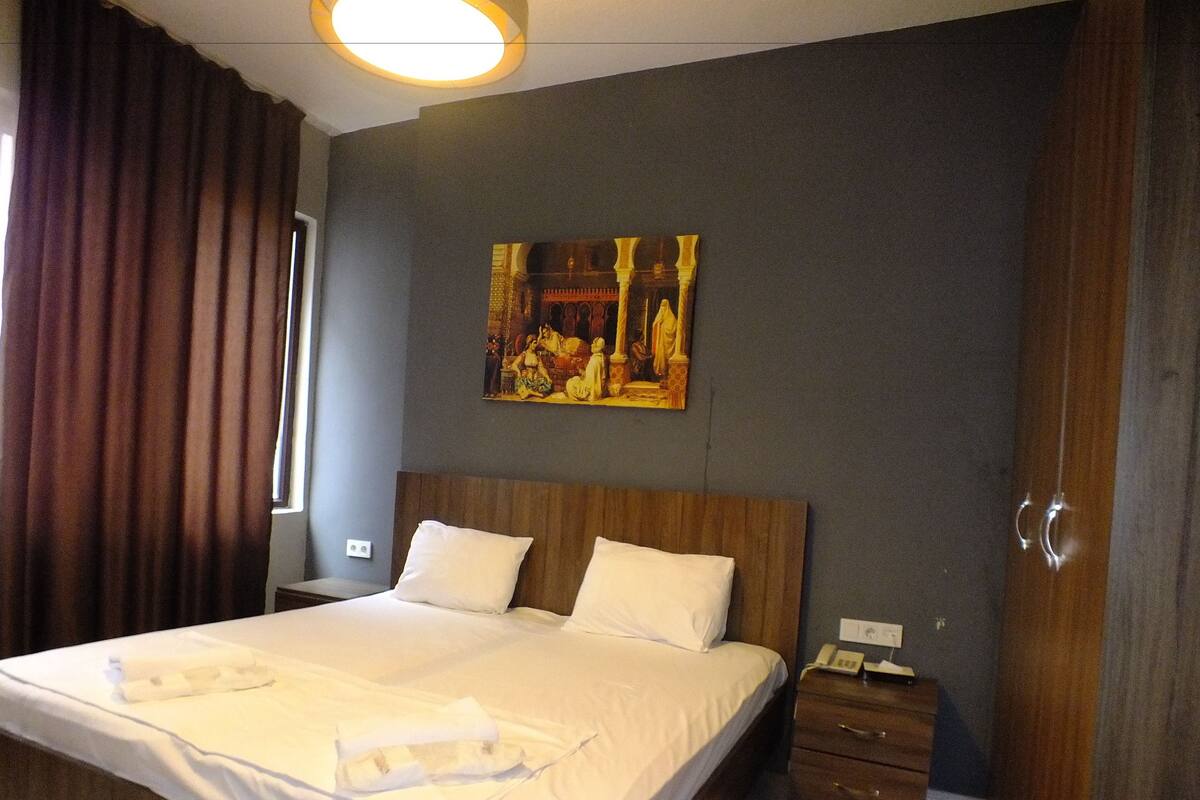 A hotel room with a large bed, a nightstand, a wooden wardrobe, and a painting on the wall.