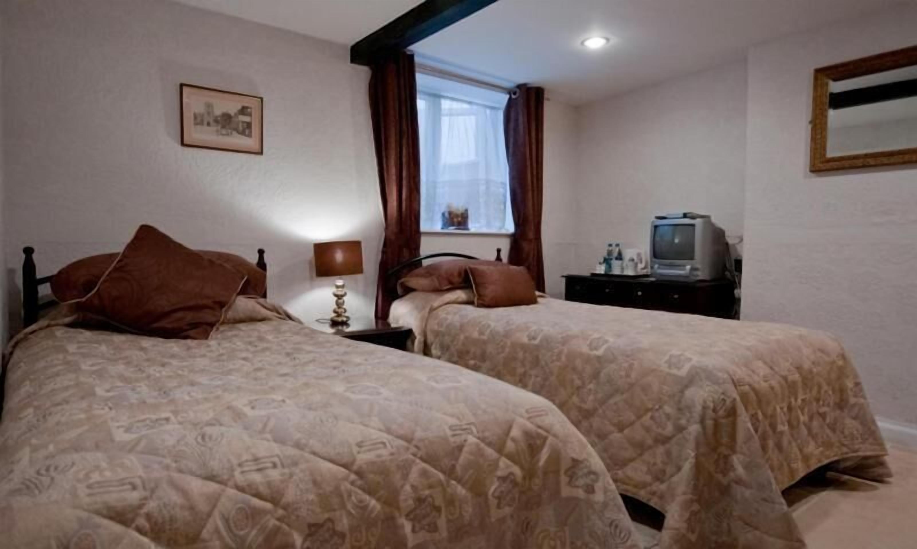 Un dormitorio con dos camas, televisión y ventana con cortinas.