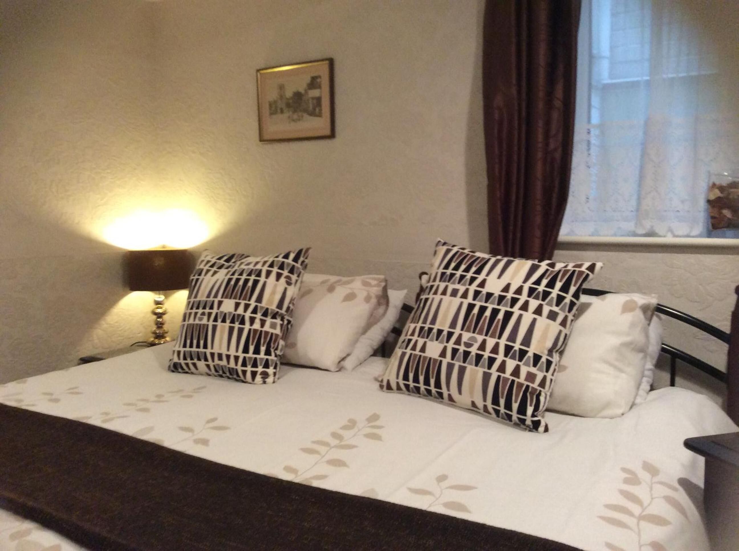 A bed with patterned pillows, a bedside lamp, and a framed picture on the wall.