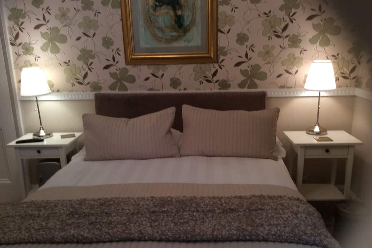 Una cama bien hecha con cabecera, dos mesitas de noche con lámparas y papel tapiz floral.