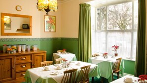 Ein Esszimmer mit grünen Wänden, einer Holzkabine zur Aufbewahrung, einer Kristallleuchtreiter und einem großen Fenster mit Vorhängen.