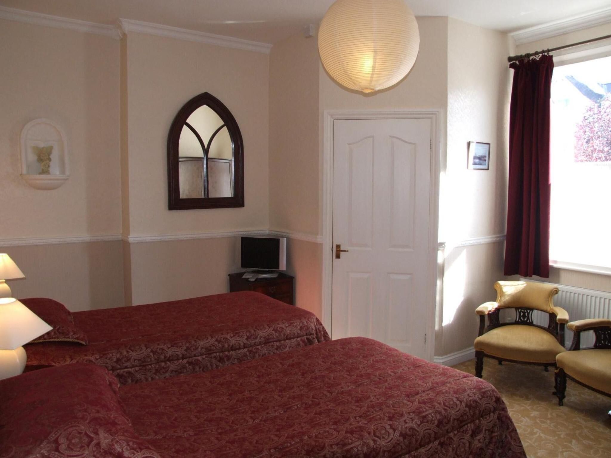 Habitación de hotel con dos camas, televisor, espejo, puerta y ventana con cortinas.
