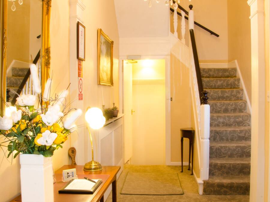 A hallway with a chandelier, a staircase, and a mirror.