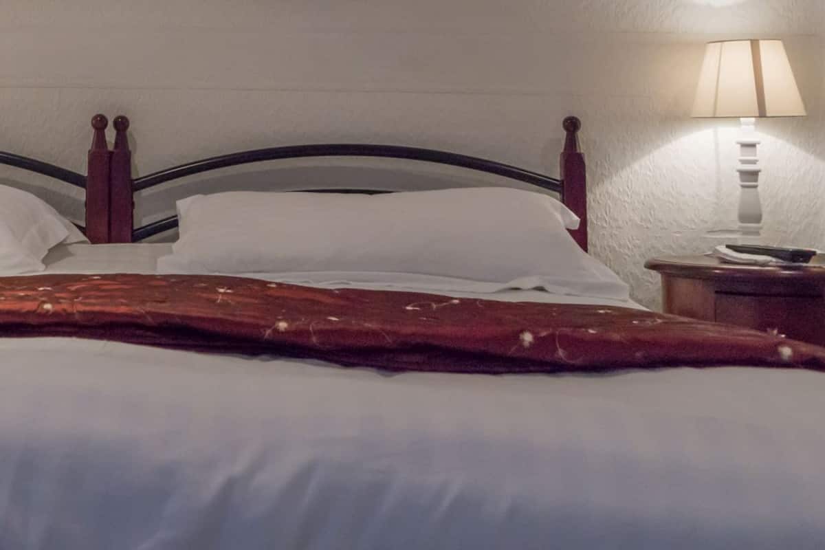 Una cama bien tendida con sábanas blancas y una manta roja, flanqueada por dos mesitas de noche con lámparas.