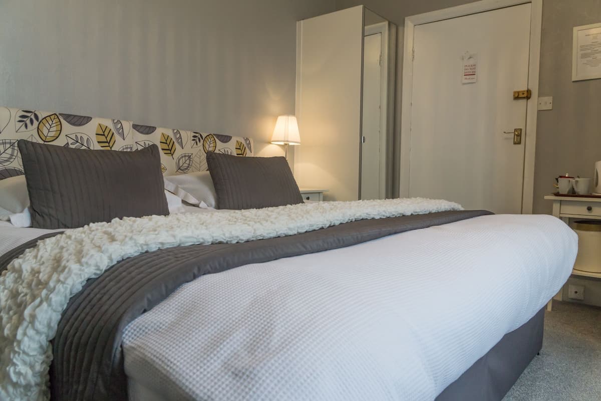 Una cama bien hecha con un edredón blanco y gris, dos almohadas oscuras y un cabecero decorativo con motivos de hojas.