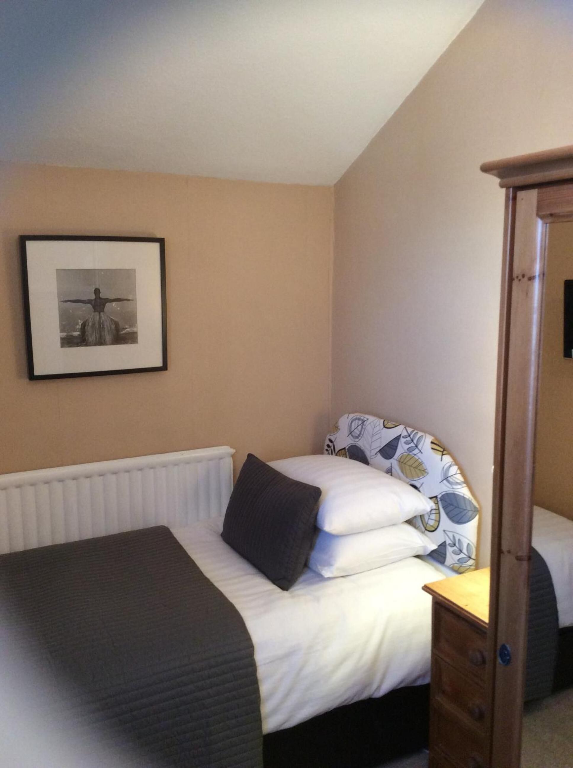 A bedroom with a bed, a radiator, a wooden wardrobe, and a framed picture on the wall.