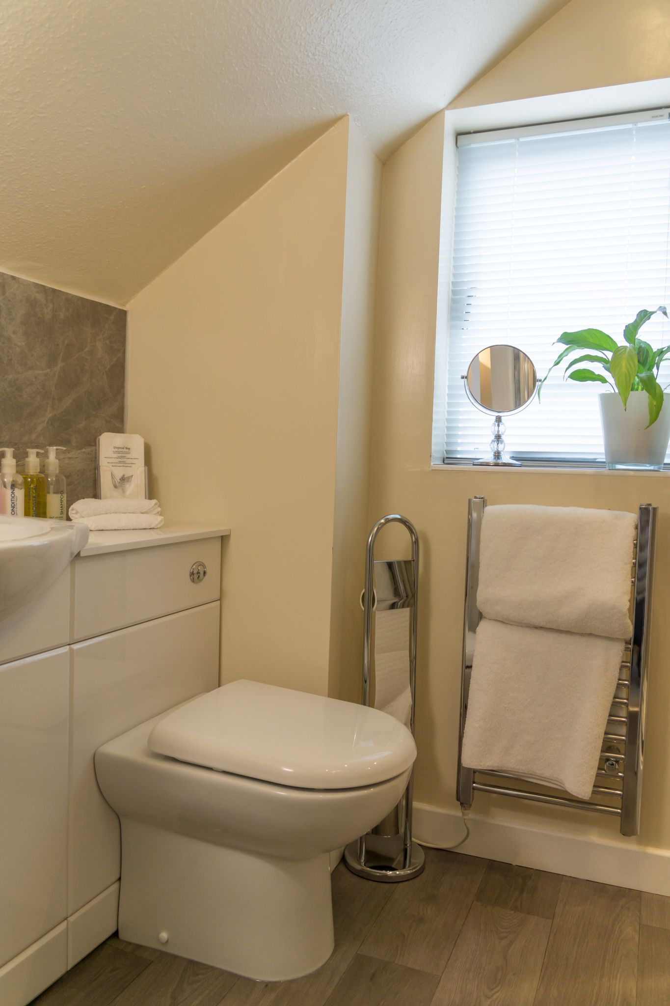 A modern bathroom with a toilet, a towel rack, a mirror, and a potted plant.