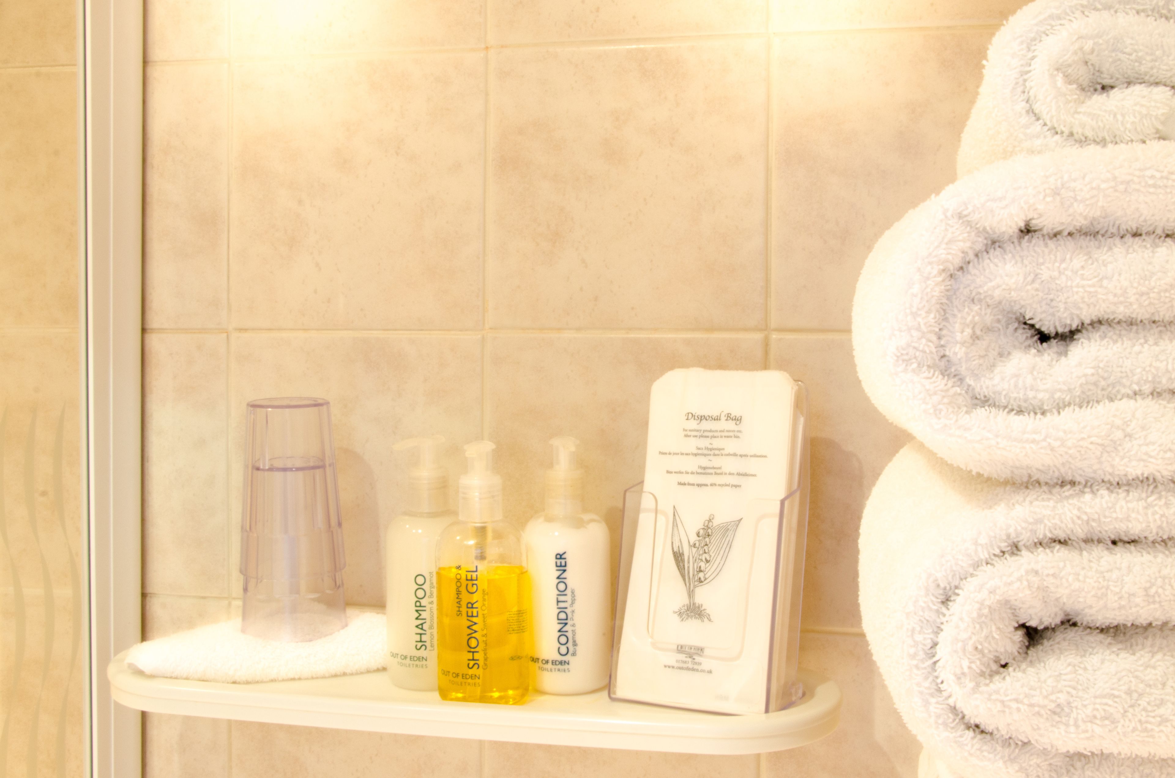 Un estante de baño con artículos de aseo como champú, gel de ducha, acondicionador y una bolsa para desechables.
