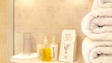 A bathroom shelf with toiletries including shampoo, shower gel, conditioner, and a disposal bag.