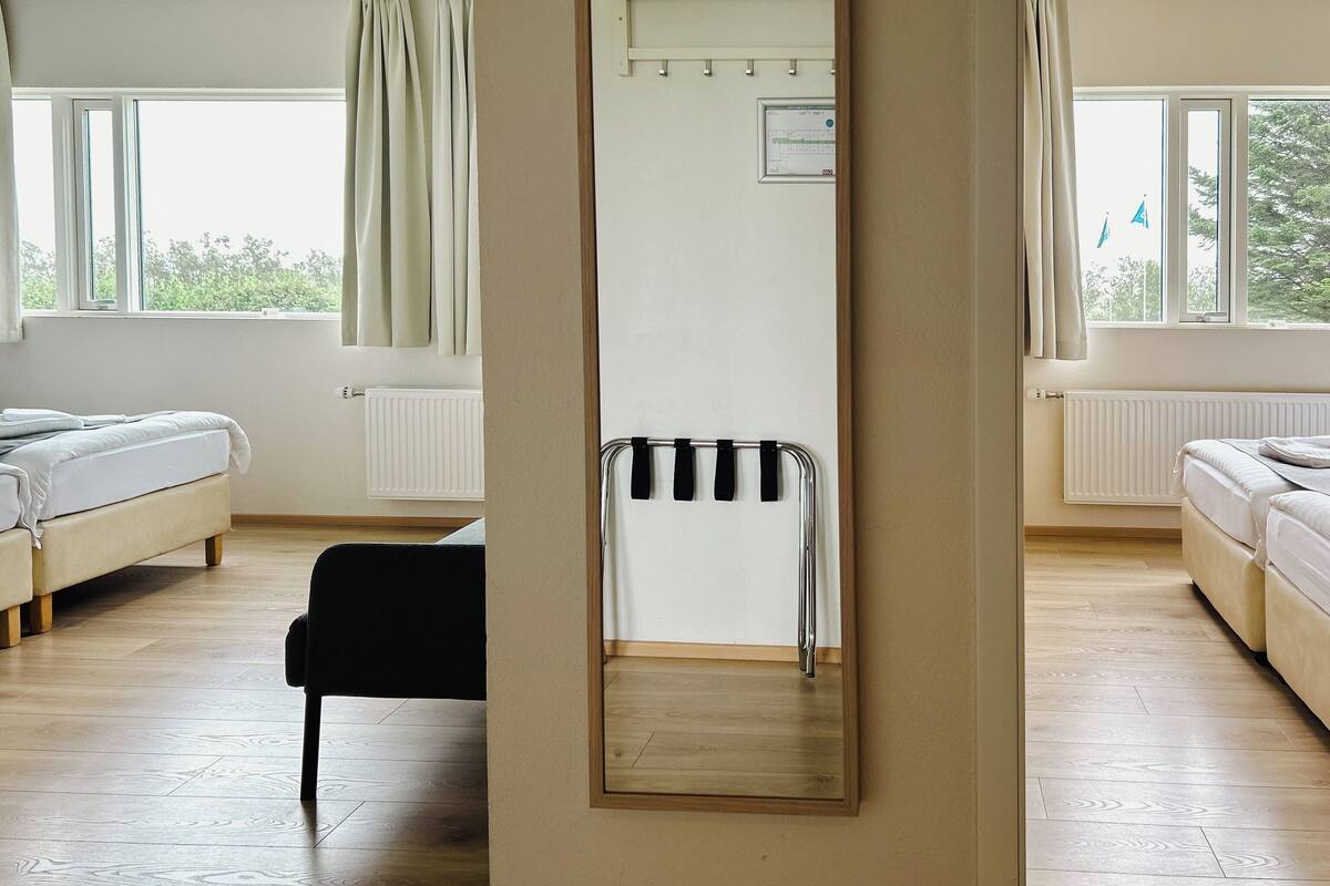 A hotel room with two beds, a black chair, a mirror, and a window with curtains.