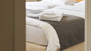 En pænt redt seng med hvide sengetøj og et gråt tæppe, et træhovedgærde og et natbord med en lampe.