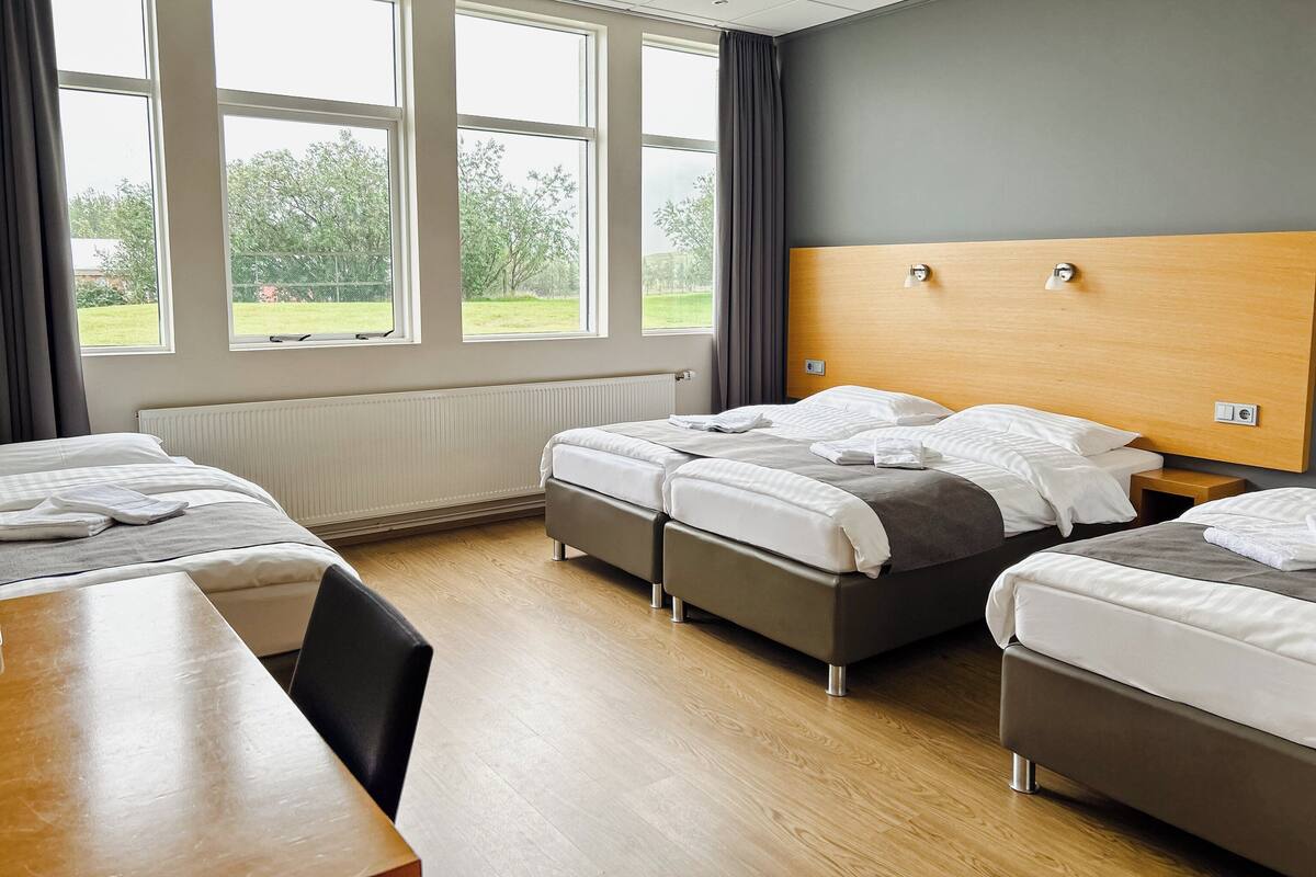 A hotel room with two beds, a wooden table, and large windows with curtains.