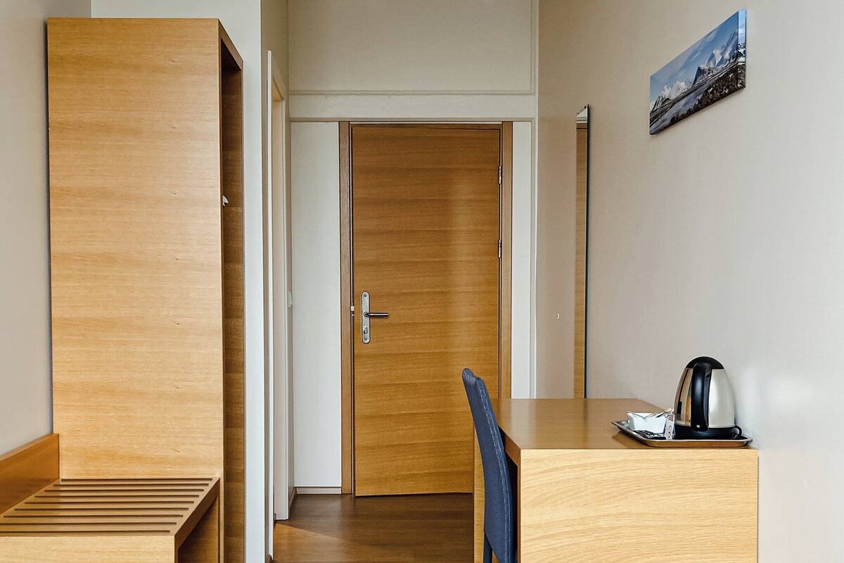 A hotel room with a bed, a desk, and a chair. There is a door leading to another room.