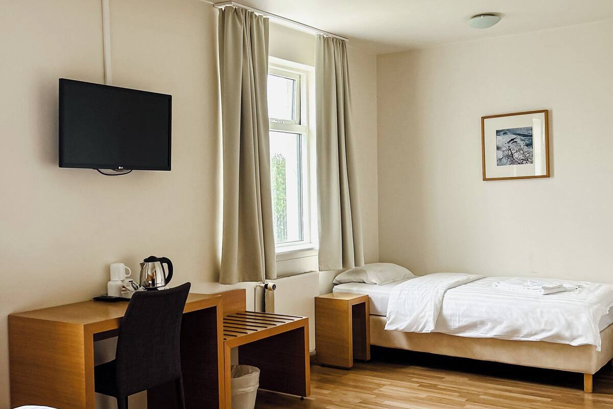 A hotel room with two beds, a desk, a chair, a television, and a window with curtains.
