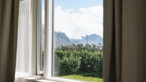 Et vindue med udsigt over et bjerglandskab og grøn bevoksning.