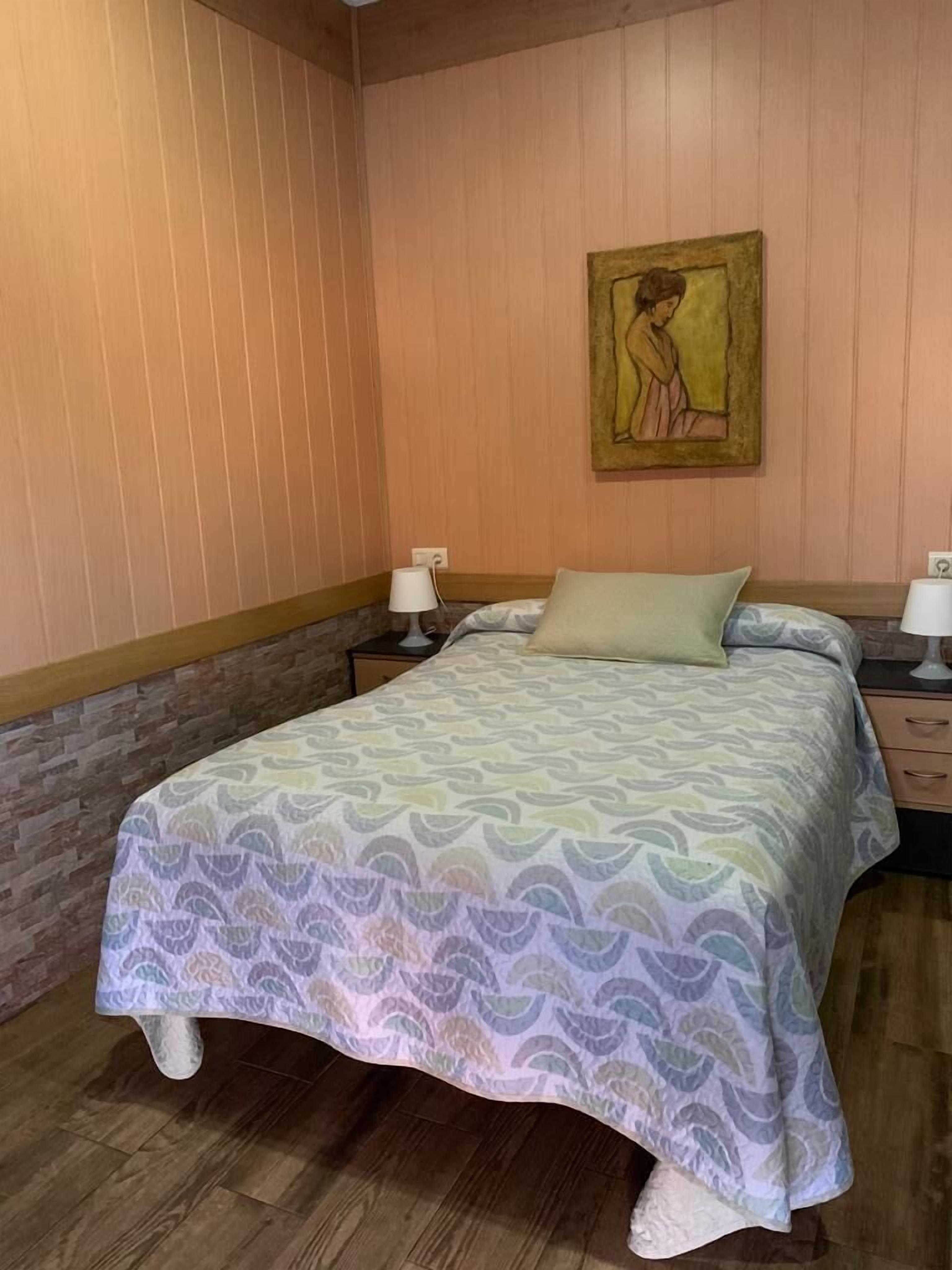 Ein Schlafzimmer mit einem Bett, Nachttischen, einem an der Wand hängenden Gemälde und Holzvertäfelung.
