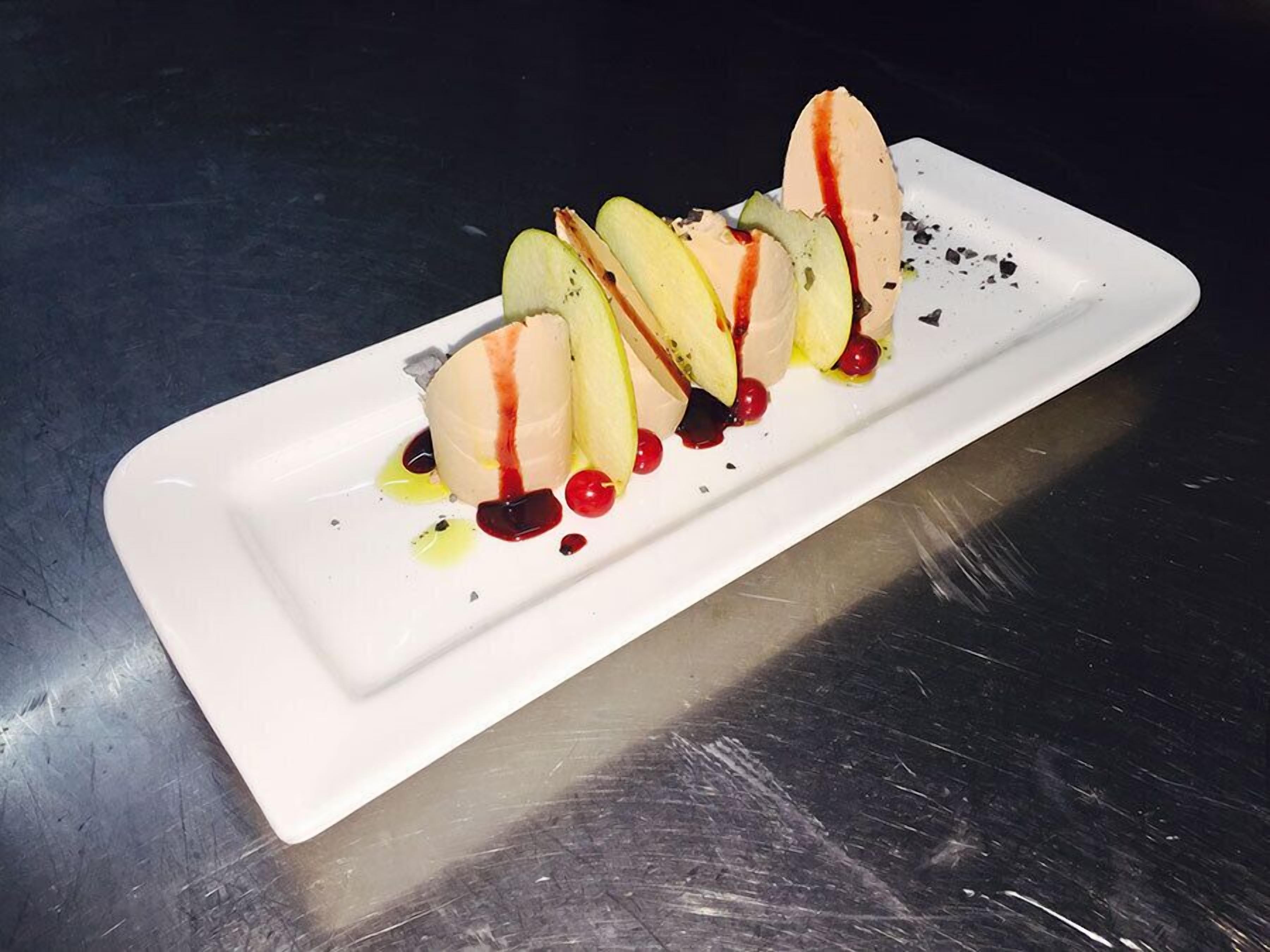Ein weißer Teller mit Dessert bestehend aus Apfelscheiben, Eis und roten Beeren, mit Soße auf einer Metalloberfläche.