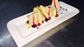 Ein weißer Teller mit Dessert bestehend aus Apfelscheiben, Eis und roten Beeren, mit Soße auf einer Metalloberfläche.