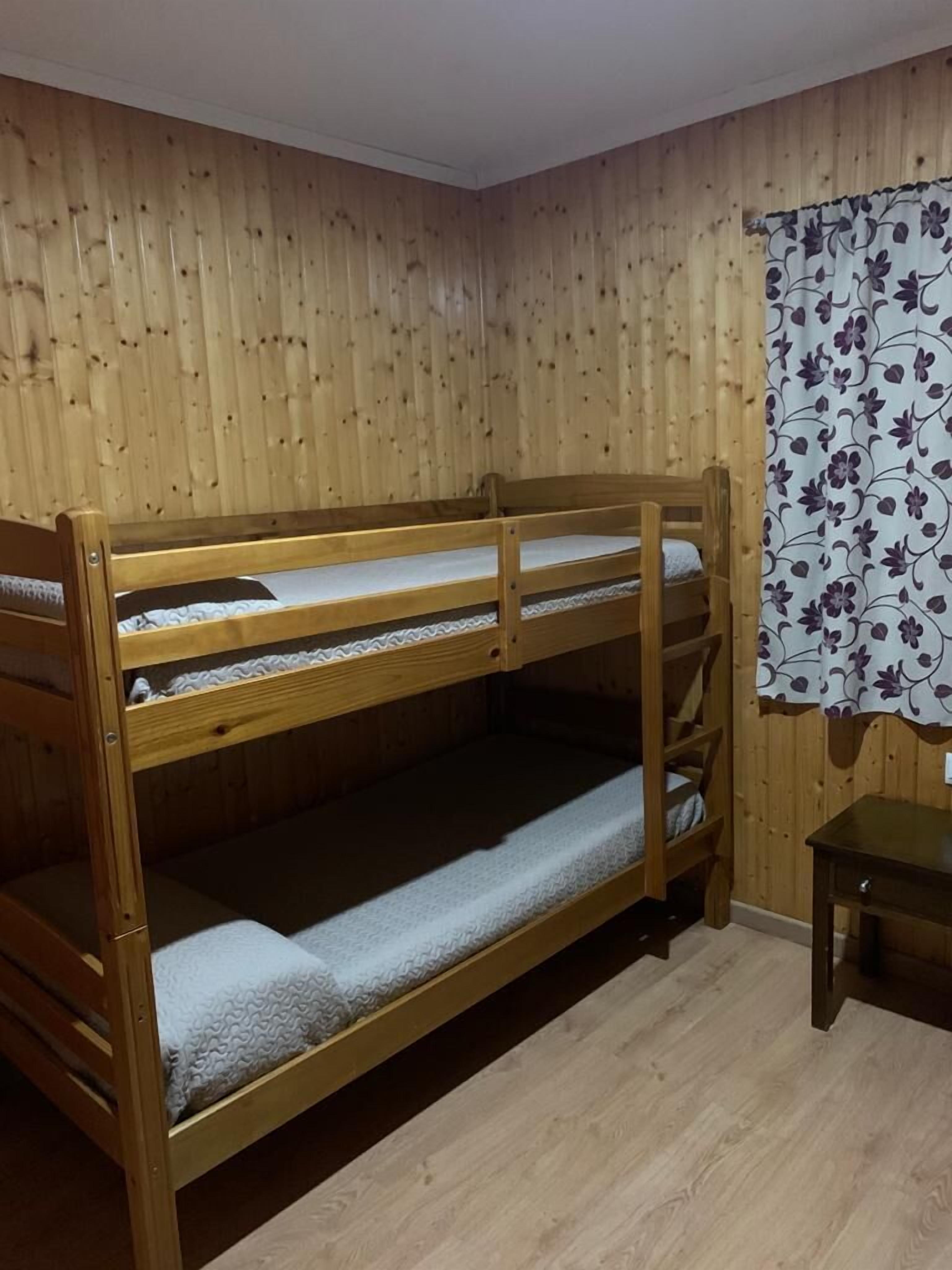 Un llit doble superposat en una habitació amb parets de fusta i una cortina floral.