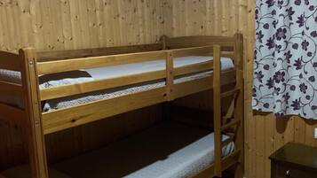 Un llit doble superposat en una habitació amb parets de fusta i una cortina floral.