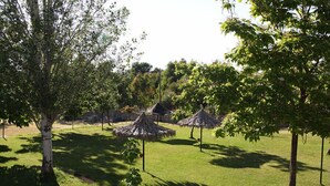 Zona verde bien cuidada con varias construcciones de techo de paja, probablemente para dar sombra o para relajarse, rodeada de árboles.