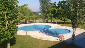 A swimming pool with a tiled edge, surrounded by grass and trees.