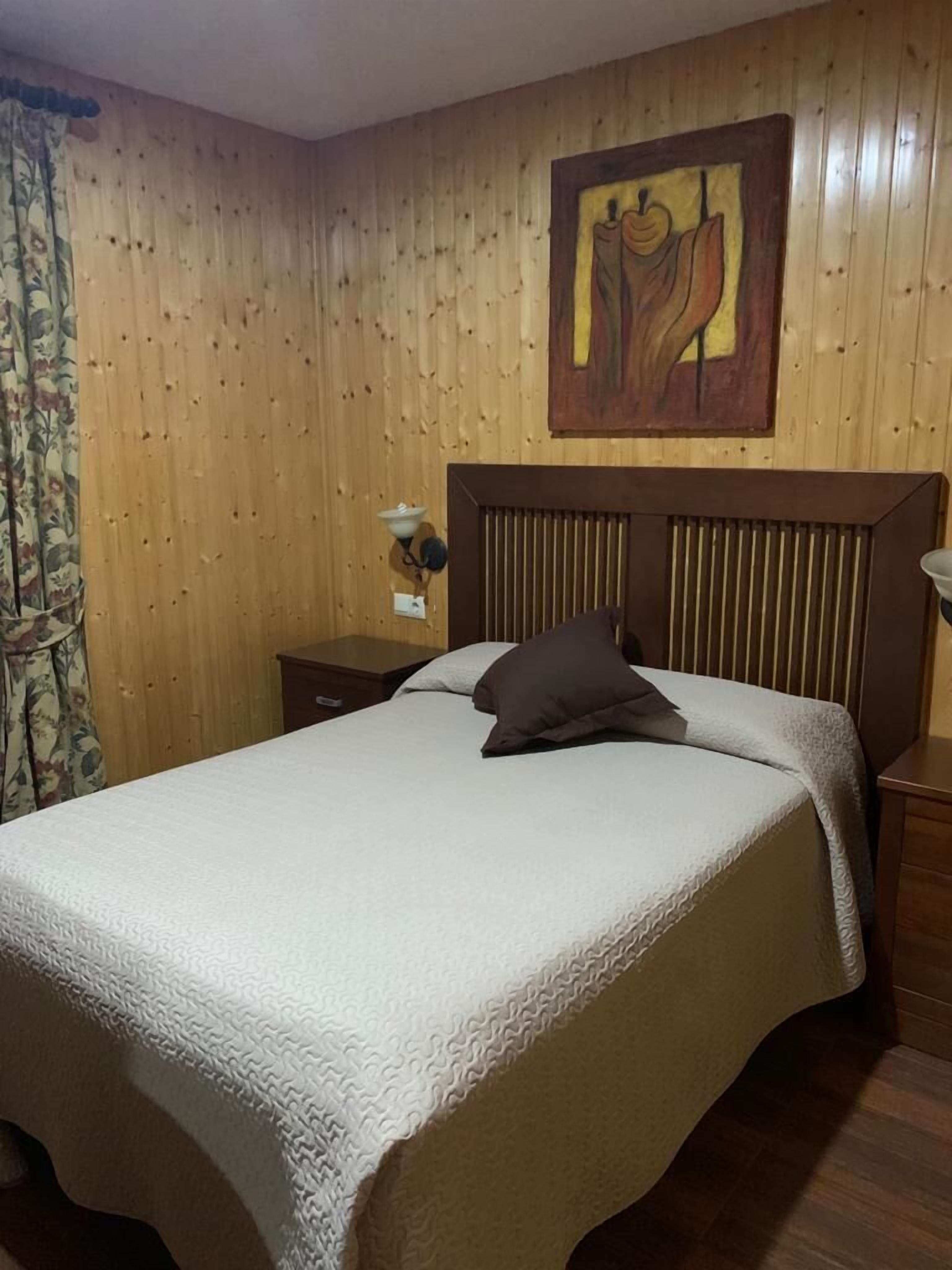 Een kamer met houten lambrisering, een bed, een nachtkastje en een kunstwerk aan de muur.