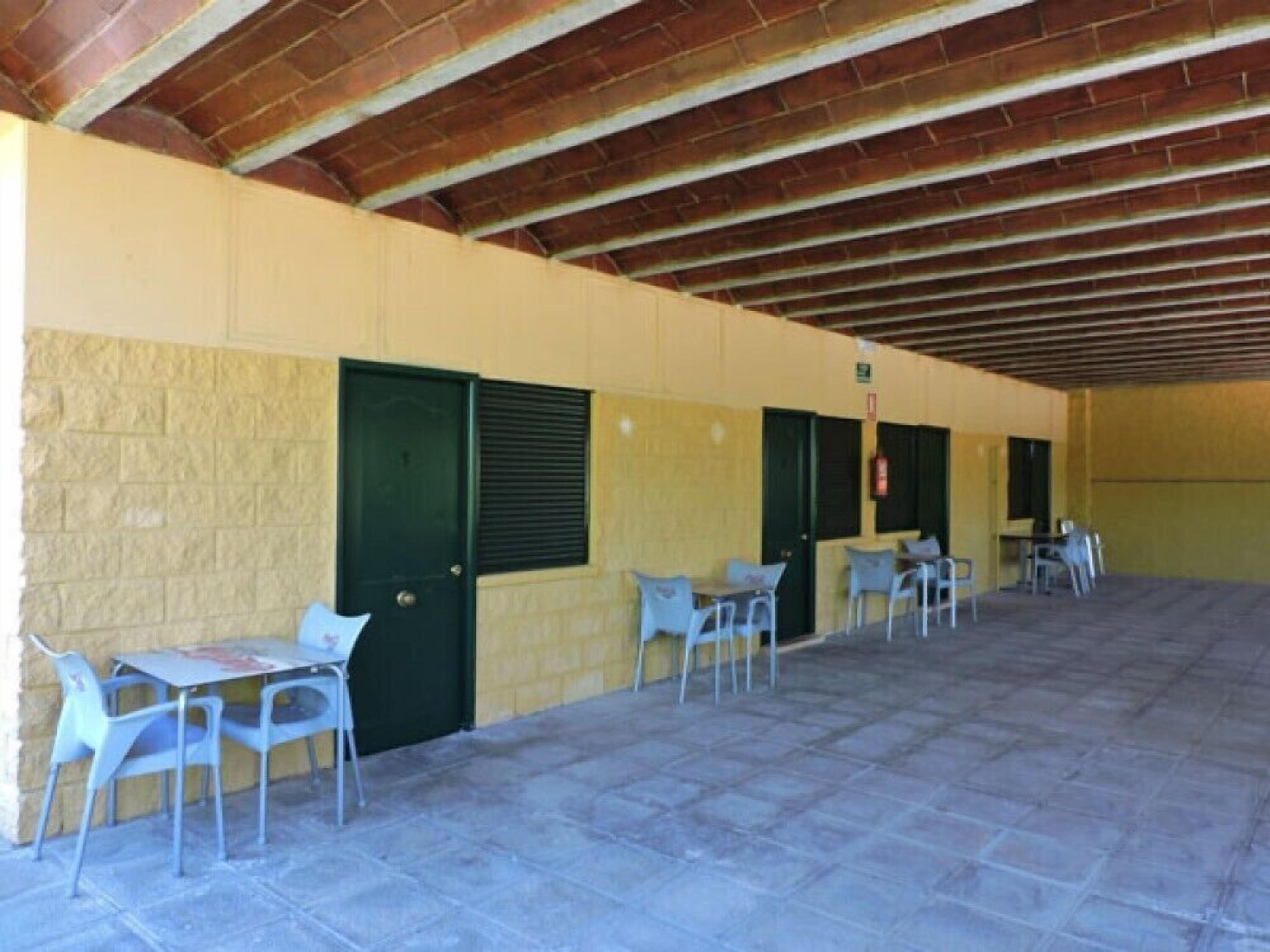 An outdoor covered patio area with tables and chairs, a brick ceiling, and a yellow wall.