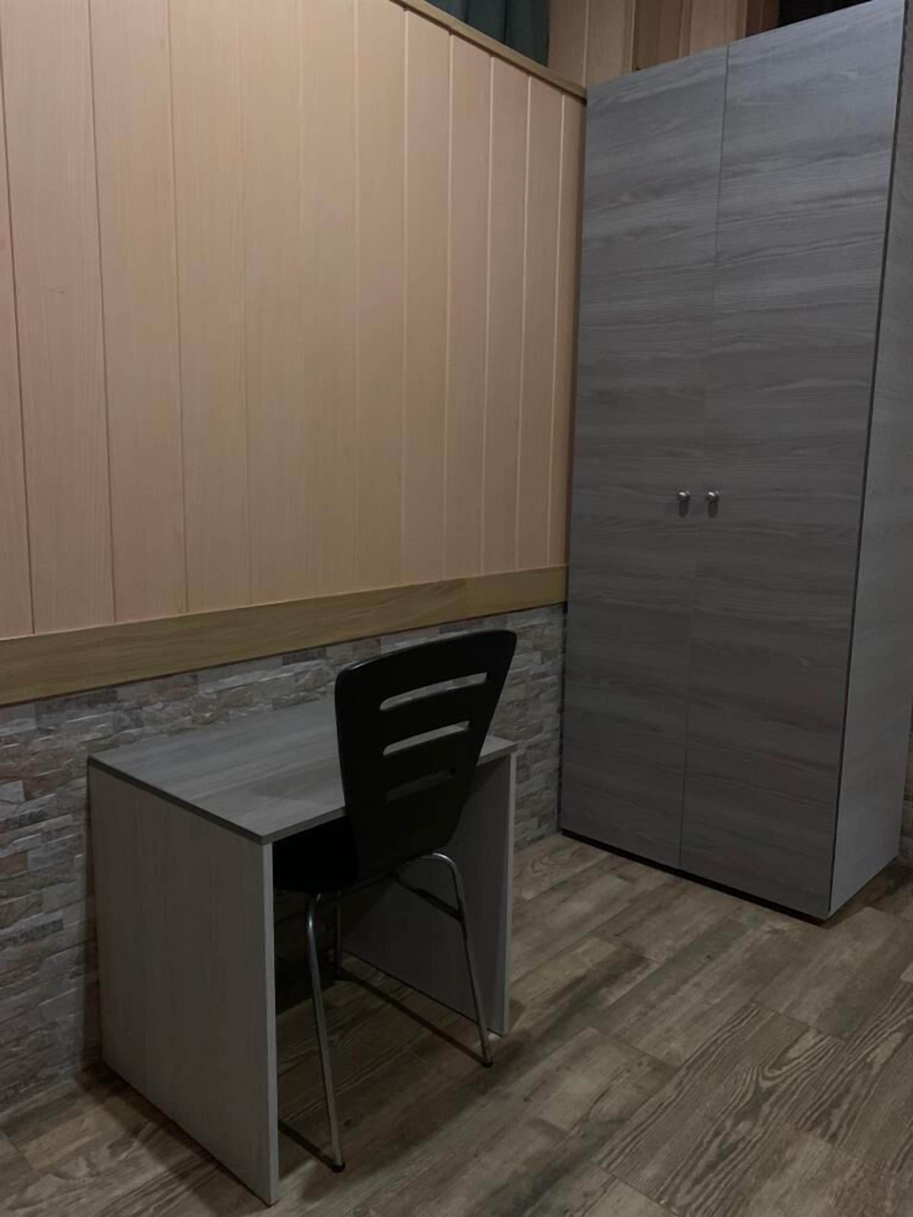 Pieni, suljettu huone, jossa on työpöytä ja tuoli, vaatekaappi ja kiviseinä.