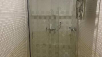 Un área de ducha pequeña y cerrada con puerta de vidrio, un banco blanco y un perchero para toallas.