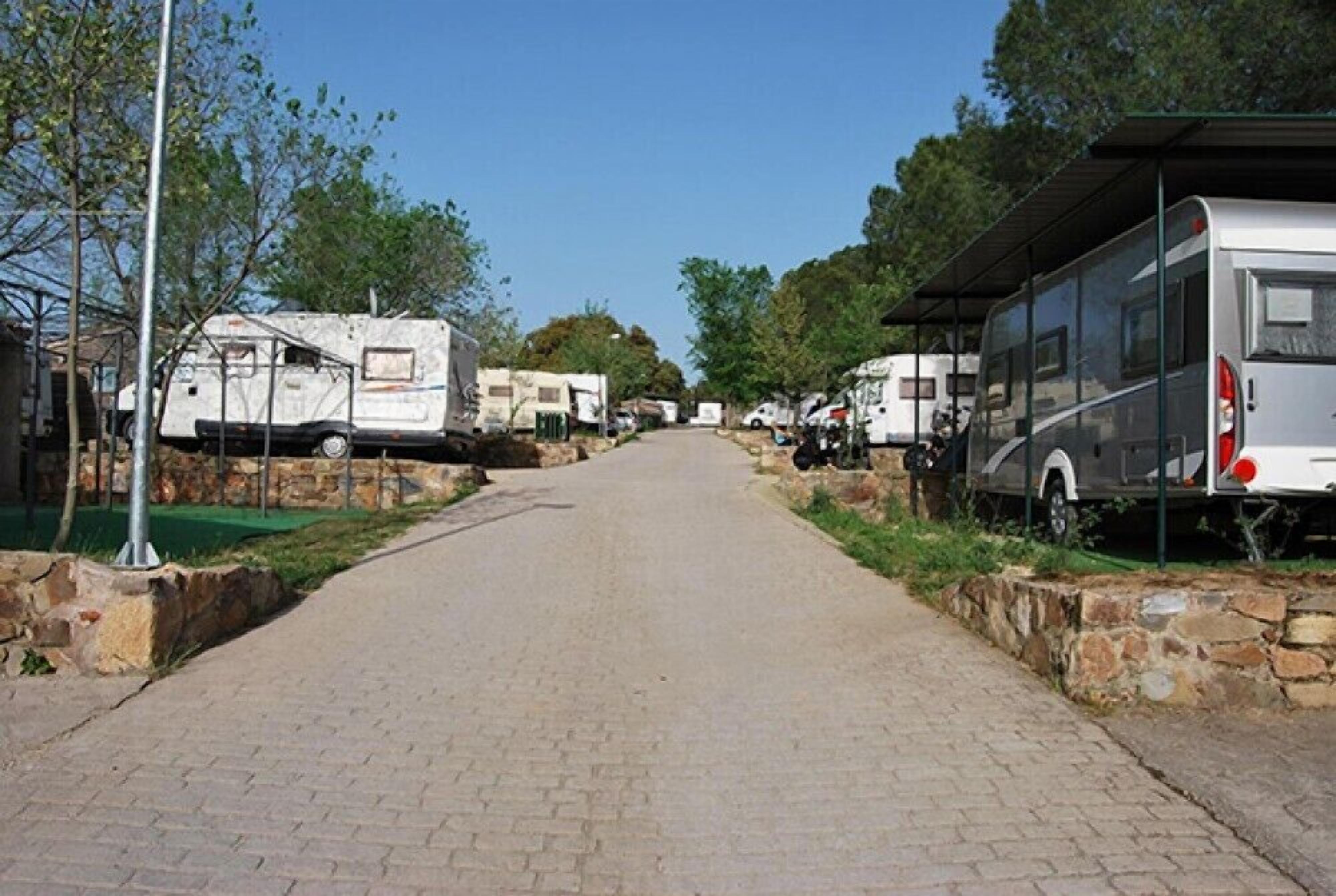 Un chemin pavé, bordé de camping-cars et de maisons mobiles, mène à une zone abritée, dont un côté est délimité par un mur de pierres.
