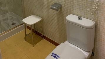 Un baño con cabina de ducha de vidrio, inodoro, un taburete pequeño y un perchero para toallas.