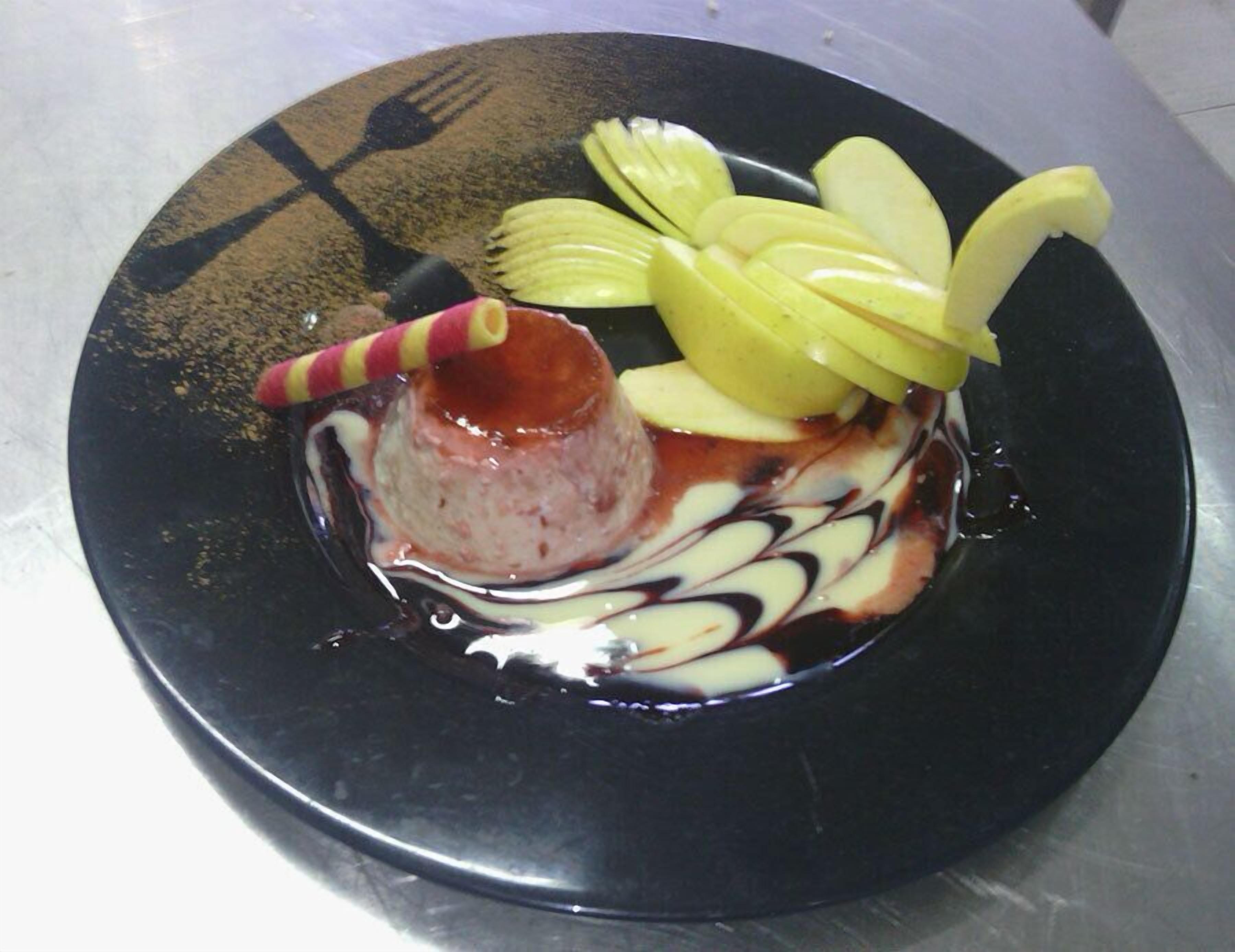 Dessert auf einem schwarzen Teller mit Karamellsauce, Apfelscheiben und einem gestreiften Strohhalm.