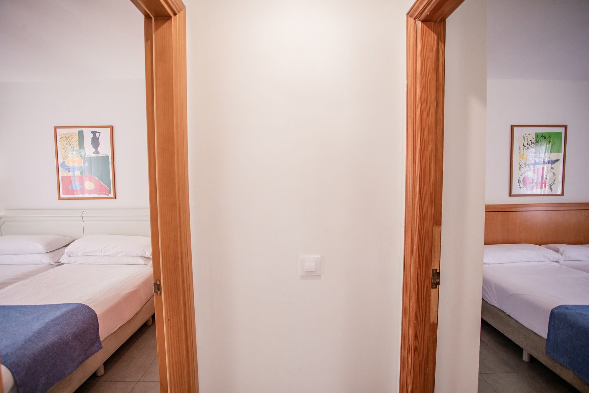 Ein Hotelzimmer mit zwei Betten, einer Holztür und zwei gerahmten Kunstwerken an den Wänden.