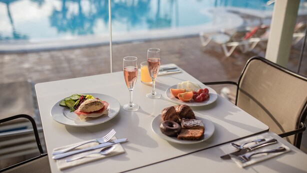 A table with a meal, two glasses of wine, and a view of a pool. - Caybeach Princess (San Bartolomé de Tirajana)