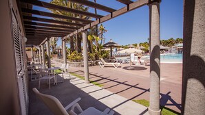 An outdoor lounge area with white chairs and tables, a pool, and palm trees. - Caybeach Princess (San Bartolomé de Tirajana)