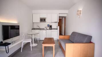 Un espacio habitable compacto con kitchenette, comedor, sofá y televisor.