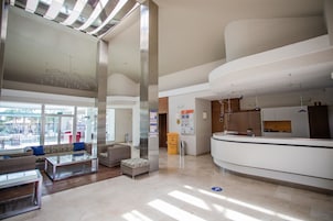 A spacious lobby with a reception desk, seating area, and large windows allowing natural light.