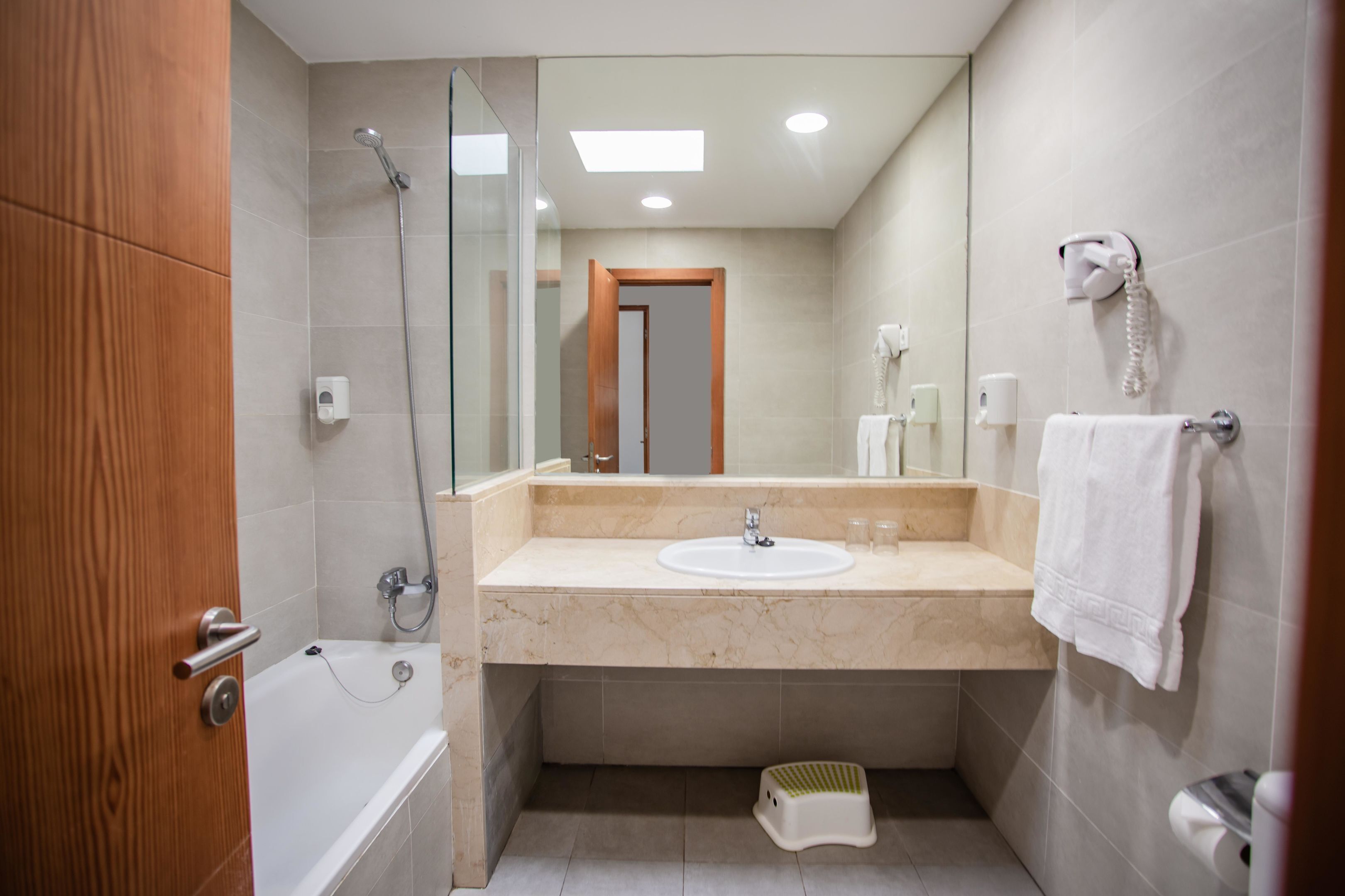 A modern bathroom with a bathtub, a sink, a glass shower enclosure, a towel rack, and a telephone.