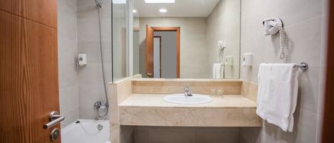 A modern bathroom with a bathtub, a sink, a glass shower enclosure, a towel rack, and a telephone.
