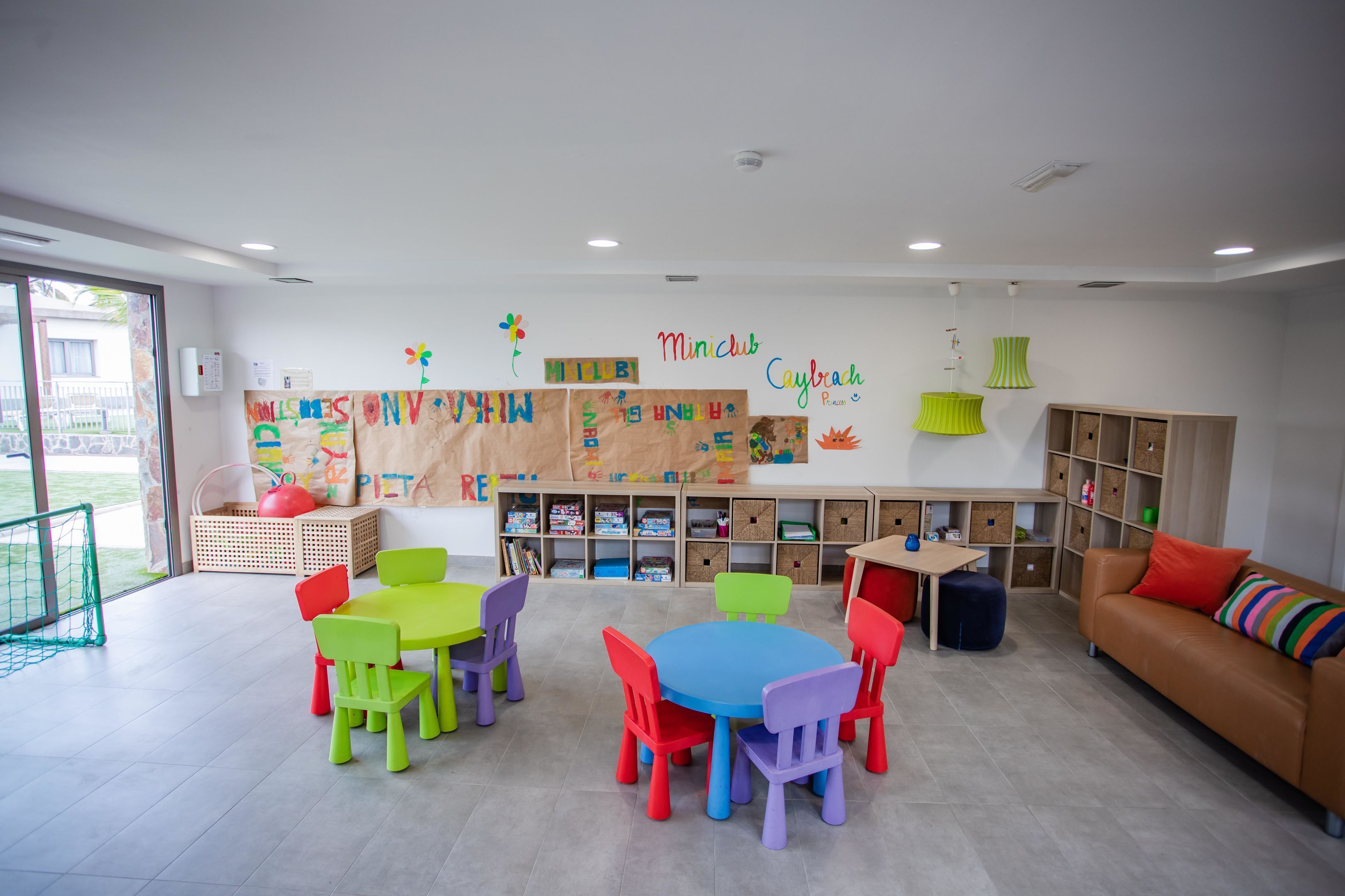 Un aula luminosa con sillas y mesas coloridas, y carteles educativos en las paredes.