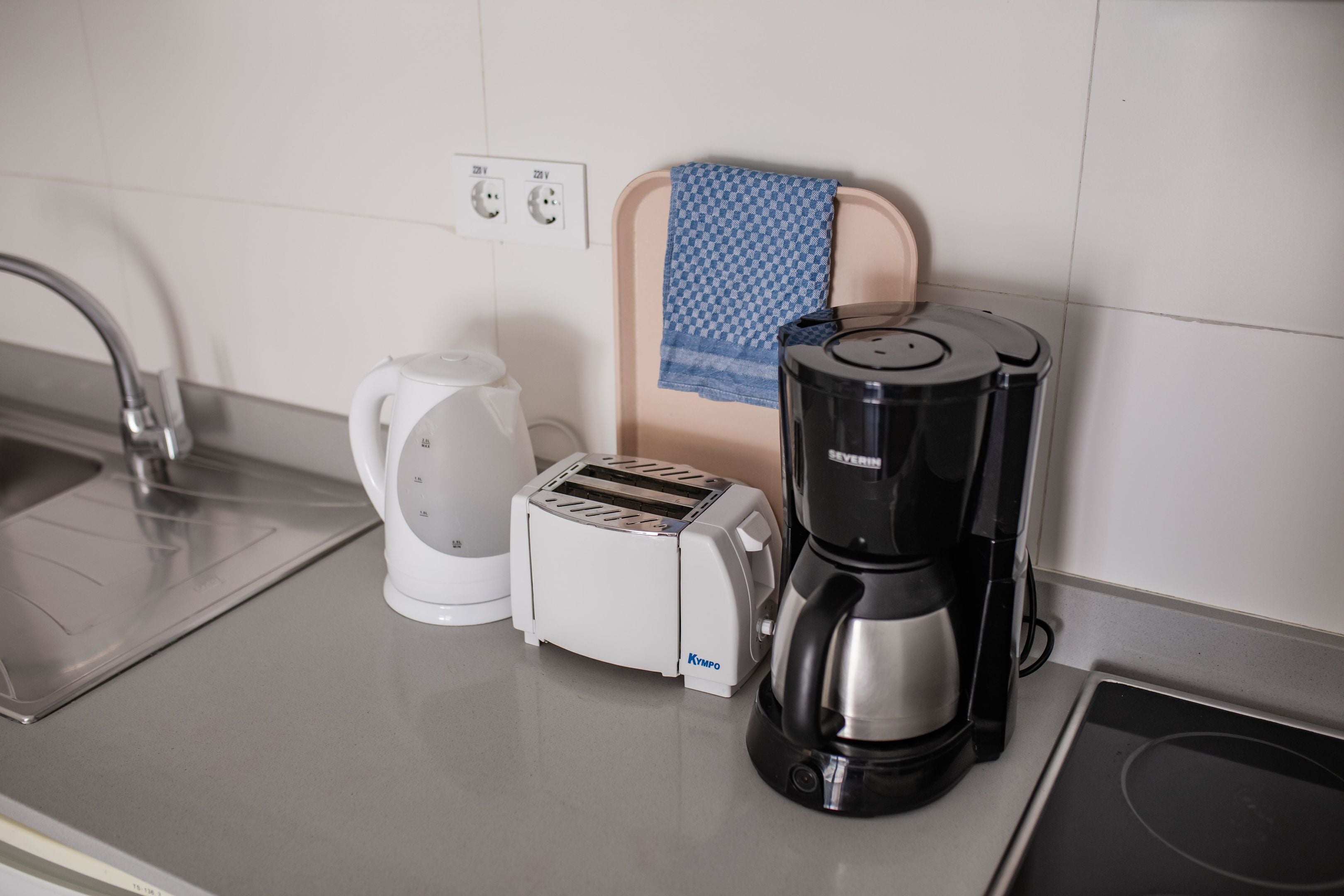 A kitchen with a toaster, coffee maker, and kettle on the counter.
