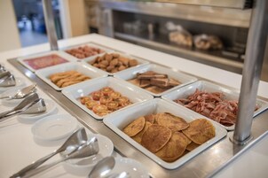 A buffet with various food items including pancakes, bacon, and tomatoes.
