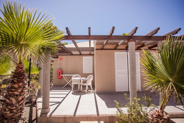 Un patio al aire libre con una pérgola, dos sillas blancas y una mesa.