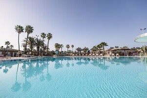 A clear blue pool surrounded by lounge chairs and palm trees.