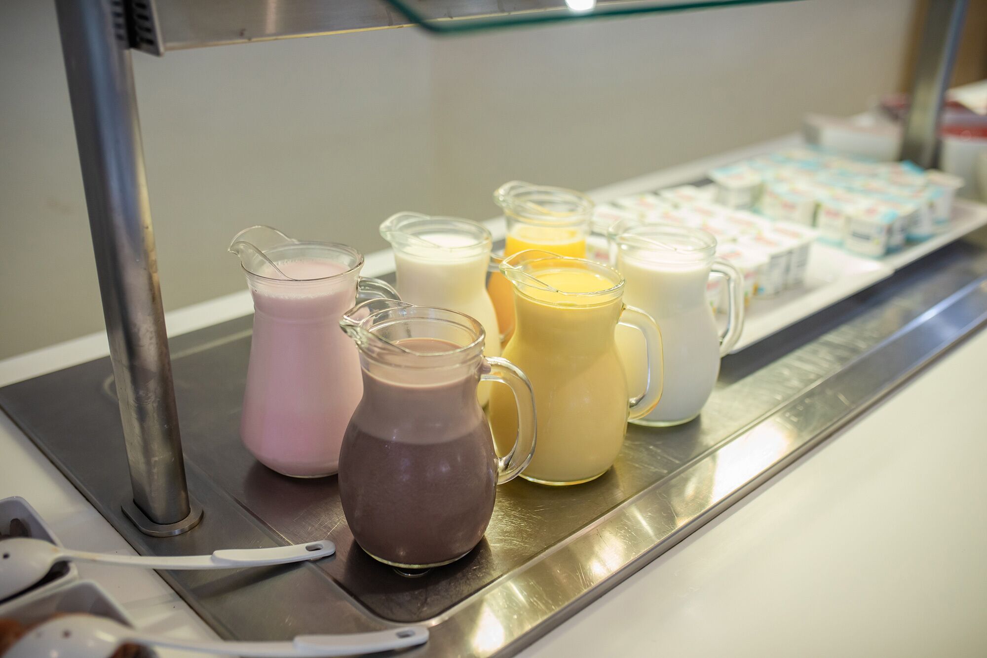 A selection of colorful beverages in pitchers and mugs on a stainless steel counter.