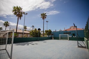 An outdoor basketball court with a goal, palm trees, and a building in the background. - Caybeach Princess (San Bartolomé de Tirajana)