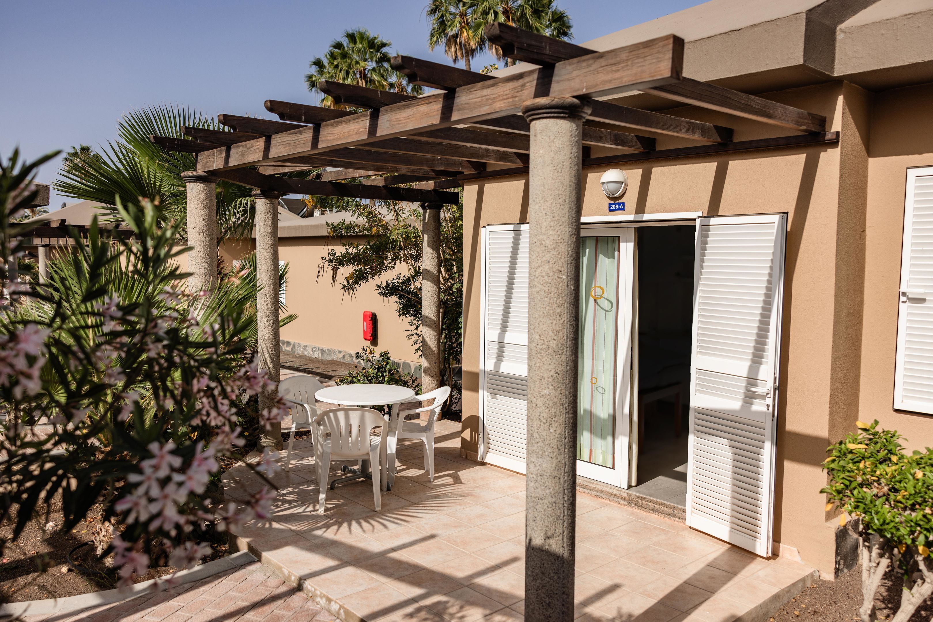Un'area patio coperta con tavolo e sedie, un pergolato e una porta che dà su una stanza.